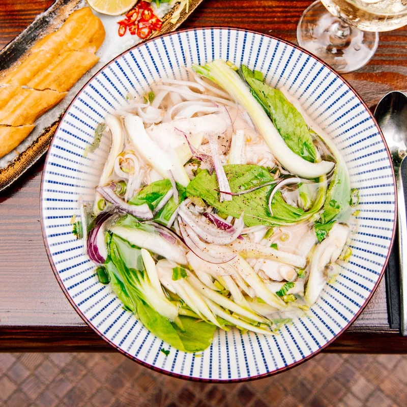 Phở gà mit Huhn und frischen Kräutern in einer blau gestreiften Schale